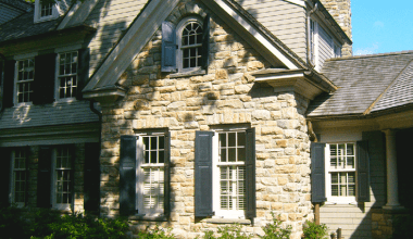 Functional shutters on stone facade of Classic Informality custom home by Daniel Contelmo Architects